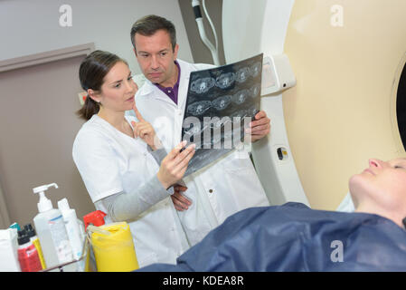 Ärzte prüfen x-ray neben Patienten, die sich einer MRT-Untersuchung Stockfoto