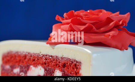 Weißer Kuchen mit Schokoladenornamenten und roter Marzipanrose auf dunkelblauem Hintergrund. Kuchen, dekoriert mit essbaren roten Rosen aus nächster Nähe Stockfoto
