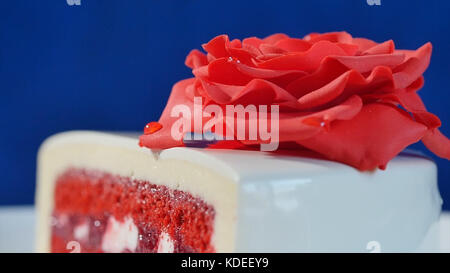 Weißer Kuchen mit Schokoladenornamenten und roter Marzipanrose auf dunkelblauem Hintergrund. Kuchen, dekoriert mit essbaren roten Rosen aus nächster Nähe Stockfoto