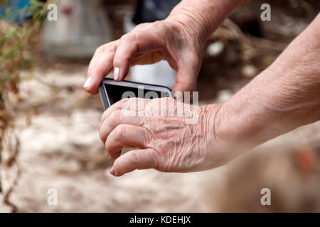 Die Hände von eine ältere Frau mit einem Mobiltelefon Stockfoto