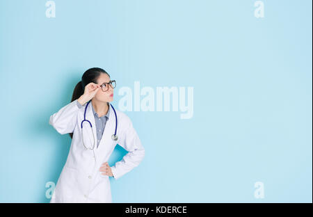 Verwirrt Schön Klinik Mädchen Arzt auf leeren Bereich vorzustellen, Patient Krankheit medizinische Problem und steht in der blauen Wand Hintergrund Büro. Stockfoto