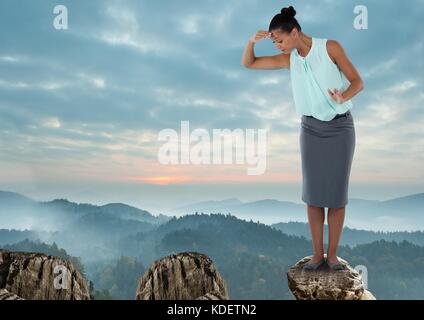 Digital composite der Geschäftsfrau, die auf der Suche nach Höhe auf Felsen in den Bergen Stockfoto