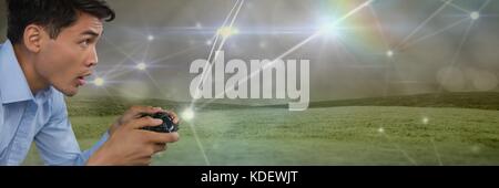 Digital composite der Geschäftsmann spielen mit Computer Game Controller mit leichten Verbindungen auf grünen Hügeln im Hintergrund Stockfoto