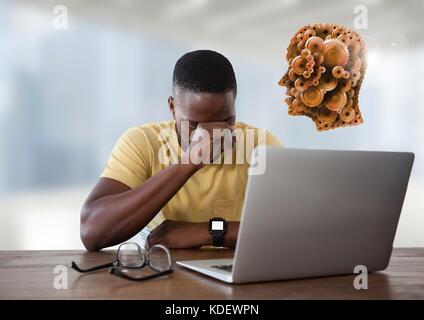 Digital composite der Geschäftsmann mit Laptop am Schreibtisch mit Rädchen Kopf Stockfoto