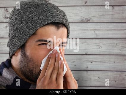 Digital composite des Menschen gegen Holz mit warmer Hut blasen Nase in Gewebe Stockfoto