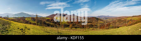 Panorama der bergigen ländlichen Gegend im Herbst. wunderschöne Landschaft mit Bergrücken und Wald mit rotem Laub an Hängen Stockfoto