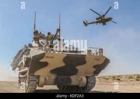 Ein AH-64 Apache-Hubschrauber der US-Armee fliegt über ein gegnerisches Force Surrogate, das während des Angriffstrainings in der Nähe der John Wayne Foothills im Fort Irwin National Training Center am 1. Juli 2017 in Fort Irwin, Kalifornien, gepanzerte russische Militärfahrzeuge nachbilden soll. (Foto von Austin Anyzeski via Planetpix) Stockfoto