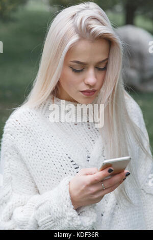 Junge schöne blonde Mädchen in warmen gestrickten Pullover verwendet ein Mobiltelefon. Stockfoto