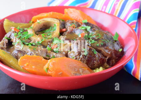 Italienisch traditionelles Kalbfleisch Gericht Osso buco mit gekochten Karotten, Kartoffeln, Sellerie in einem roten Keramik Schüssel Stockfoto