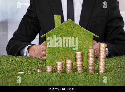 Geschäftsmann Holding umweltfreundliche Haus vor Stapel von Münzen über Gras Stockfoto