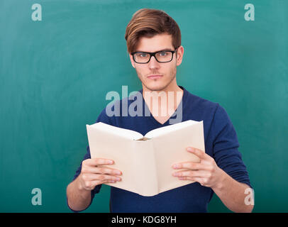 Porträt eines jungen Studenten, Buch vor grünen Tafel hält Stockfoto