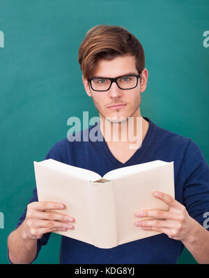 Porträt eines jungen Studenten, Buch vor grünen Tafel hält Stockfoto