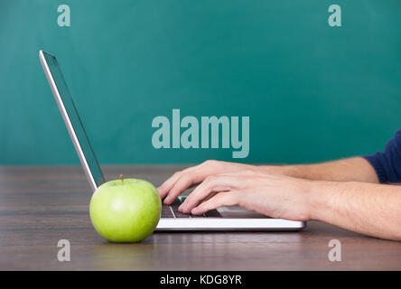 Nahaufnahme der Person die Hand mit Laptop mit grünem Apfel auf Schreibtisch Stockfoto
