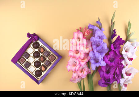 Wunderschöne gladiolen Blumen auf Gelb mit köstlichen Pralinen in Geschenkbox. Stockfoto