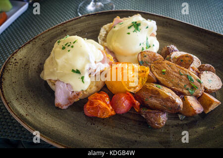 Köstliche Benedikt Eier mit Baked patatoes und Tomaten auf dunklen Teller serviert Stockfoto