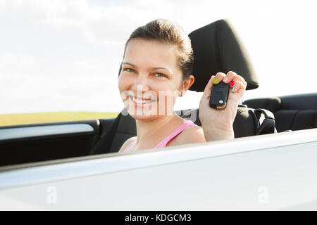 Glückliche junge Frau im neuen Auto mit Schlüssel Stockfoto