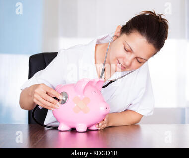 Ärztin holding Stethoskop zu rosa Sparschwein Stockfoto