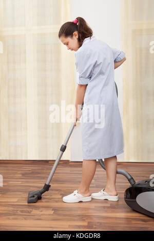 Junge maid Reinigung Boden mit Handstaubsauger Stockfoto