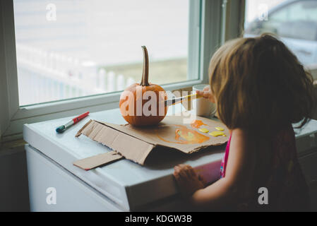 Ein kleines Mädchen malt Kürbisse im Herbst Aktivitäten. Stockfoto