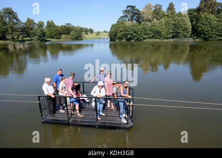 Besucher nutzen die von Capability Brown entworfene Kettenfähre oder Seilfähre über den See im Compton Verney House, Warwickshire, England Stockfoto