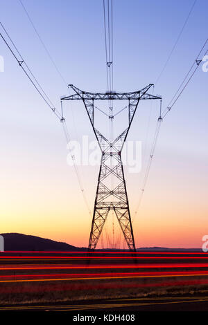 Lange Exposition von Strommasten neben der Autobahn bei Sonnenuntergang mit Autos. Stockfoto