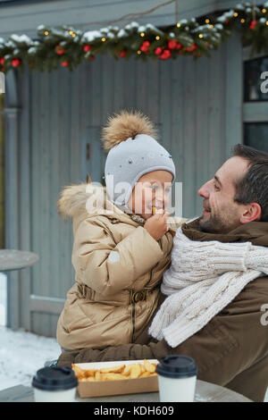 Liebevoller Vater hielt seine bezaubernde Tochter essen Snack auf festliche Veranstaltung im Freien Stockfoto