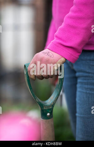 Gardener wearing pink gardening gloves holding a garden fork handle. Selective focus. Shallow DOF Stockfoto