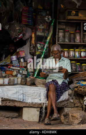 Ein Mann eine Zeitung lesen in seinem Geschäft in Fort Kochi Stockfoto