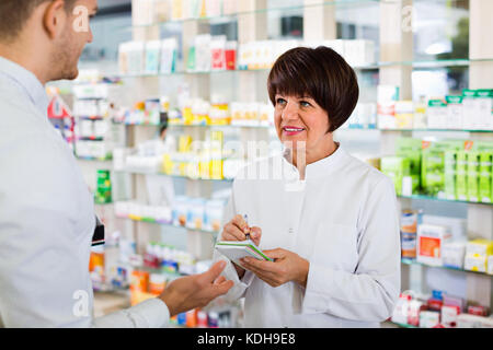 Fröhliche positive Frau Apotheker im weißen Mantel Kunden los im Drug Store zu finden Stockfoto