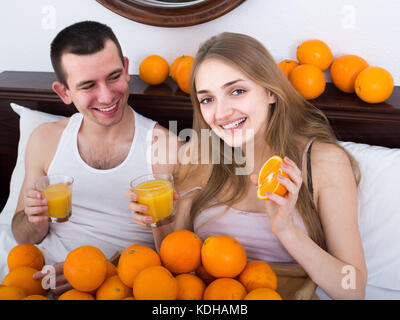 Happy europäischen Mann und Freundin trinken gepressten Orangensaft im Bett Stockfoto