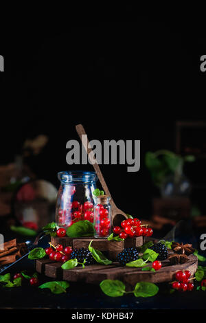 Glas mit frischen Johannisbeeren und Blackberry mit Löffel aus Holz auf einem schwarzen Hintergrund. Labor und Wissenschaft Konzept. magische Stillleben mit Zimt und ein Stockfoto