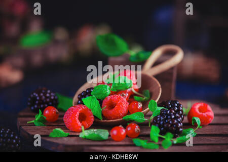 Sommer noch Leben mit Beeren in eine grosse Löffel aus Holz auf einem dunklen Hintergrund. Himbeere und Blackberry mit grüner Minze. Stockfoto