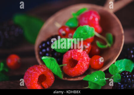 Close-up kleine hölzerne Schüssel mit frischen Himbeeren, Heidelbeeren, Johannisbeeren und Minze. Dunkle essen Fotografie mit kopieren. Stockfoto