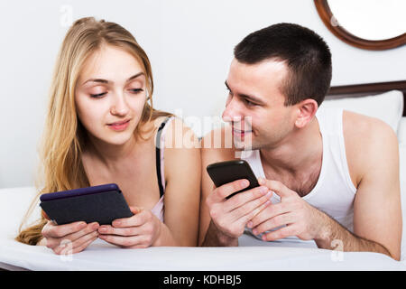 Junge Familie Paar Entgraten mit Tabletten im Schlafzimmer Innenraum. Im Mittelpunkt der Mensch Stockfoto