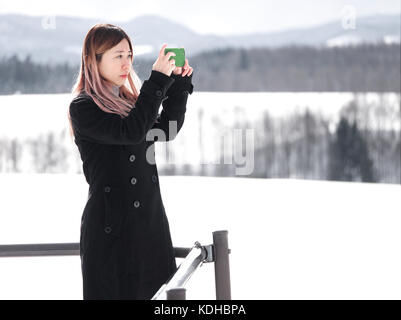 Asiatischer chinesischer Tourist, der im Winter mit einem Handy in Biei, Hokkaido, Japan, fotografiert Stockfoto