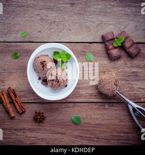 Schokoladeneis in Weiß Schüssel mit frischer Pfefferminze Blätter und dunkle Schokolade setup auf schäbige Holz- Hintergrund. Sommer- und Dessertkarte co Stockfoto