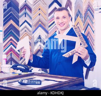 Fröhlicher positiver Mann Arbeiter holding Bilderrahmen details zu Counter im Studio Stockfoto