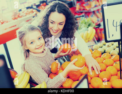 Lächelnde junge Mutter und ihre kleine süße Tochter Einkauf süßen Mandarinen am Markt. Fokus auf Mädchen Stockfoto