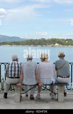 Zwei Ehepaare oder vier Rentner oder ältere Menschen sitzen auf einer Bank mit Blick auf das Meer beim Urlaub in Griechenland auf einer Kreuzfahrt als Freunde. Stockfoto