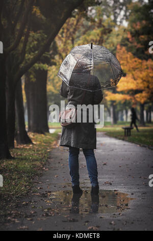 Frau mit transparenten Regenschirm an einem regnerischen Tag in einer Pfütze Stockfoto