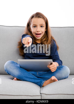 Happy kleines Mädchen sitzt auf einer Couch und mit einem Tablet Stockfoto