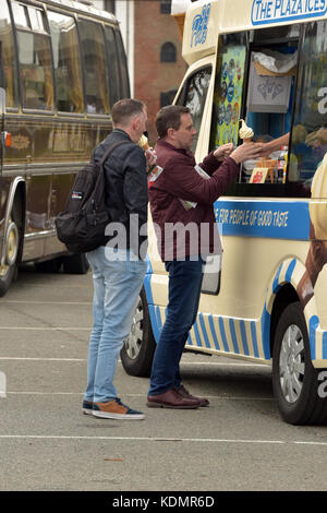 Zwei Männer, die in eine Warteschlange für ein Eis an einem Oldtimer Bus Event auf der Insel Wight. Guys selbst der Kauf eines Eis am Stiel oder Cornet aus dem ice cream van Stockfoto