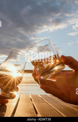 Niedriger Winkel Nahaufnahme zwei Hände, die alkoholische Getränke draußen an Deck beim Sonnenuntergang-Porträt rösten. Stockfoto