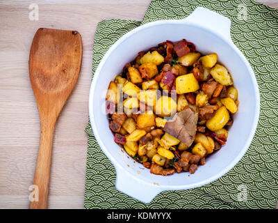 Französische Küche lardons - gebratene cubed Schweinebauch, Speck und die gewürfelten Kartoffeln mit Thymian, Lorbeerblätter und galic in einer weißen Schüssel auf hölzernen Tisch flach eingestellt Stockfoto