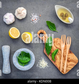 Basilikum Vinaigrette Dressing Zutaten auf dunklen konkreten Hintergrund mit Flach frisches Basilikum Blätter, Zitronenscheibe, natives Olivenöl extra ein Stockfoto