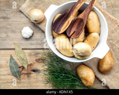 Frische organische Kartoffeln in Hanf sack Sack mit Zutaten und Kräuter Lorbeerblätter, Fenchel, Zwiebel und Knoblauch auf rustikalen Holztisch Vorbereitung für Cookin Stockfoto