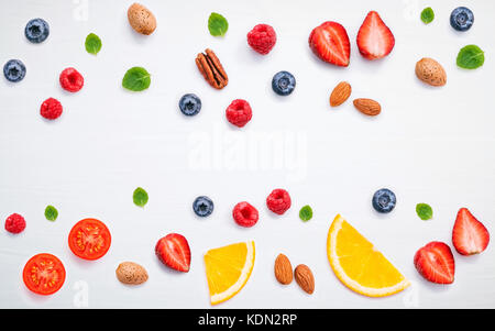 Bunte verschiedene Früchte Himbeere, Heidelbeere, Erdbeere, Orange Slice, Pecan, Mandeln, Tomaten und Pfefferminze Blätter setup auf weißem Hintergrund. Summe Stockfoto