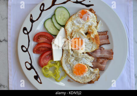 Platte dekoriert mit Frühstück - Spiegeleier, Speck und frischem Gemüse serviert. Stockfoto