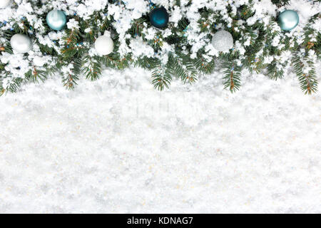 Weihnachten Hintergrund mit Weihnachten Tannenbaum Grenze dekoriert mit Christbaumkugeln und Schneeflocken auf einer dicken Schicht aus irisierendem Schnee. Stockfoto