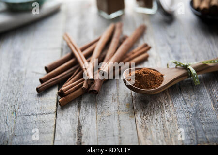 Löffel aus Holz mit gemahlener Zimt auf Holzmöbeln im Landhausstil Oberfläche mit Zimtstangen gefüllt. Stockfoto